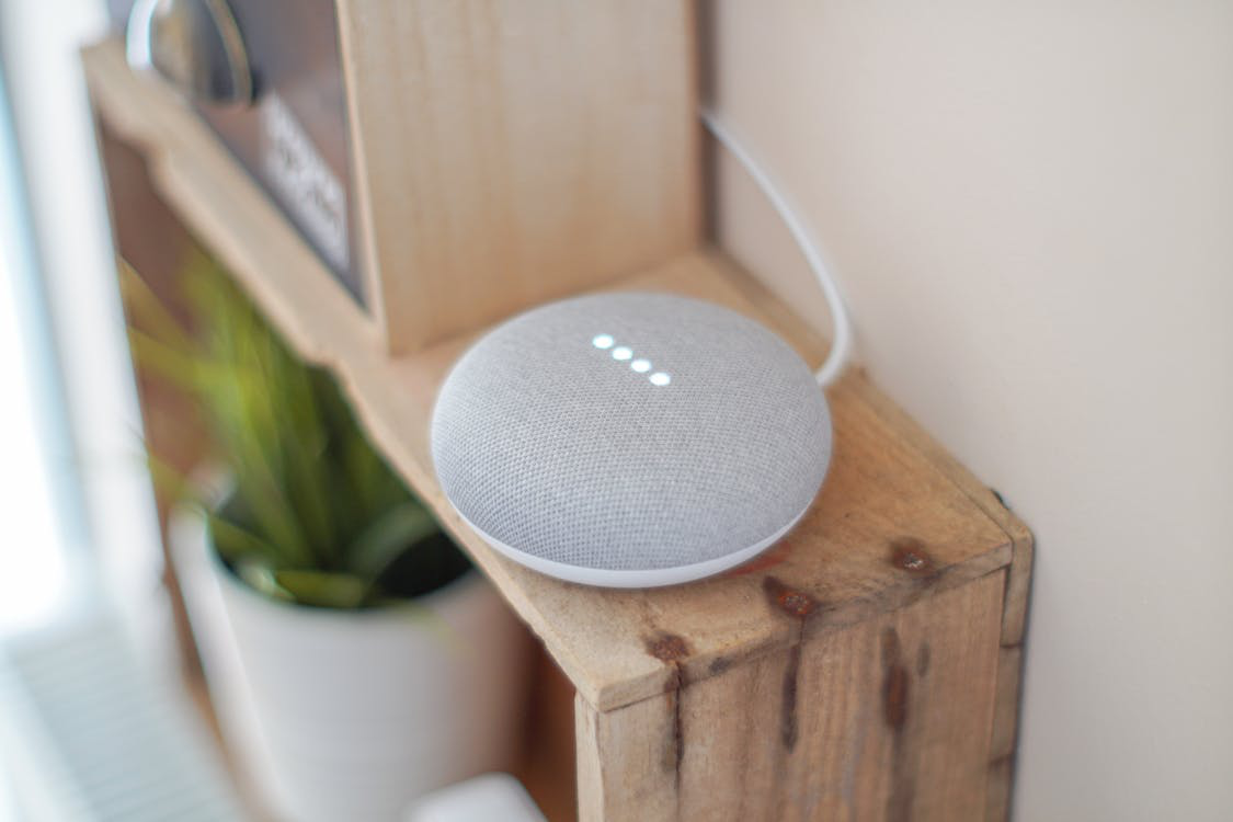 A close-up of a gray Google Nest smart speaker on a wooden shelf