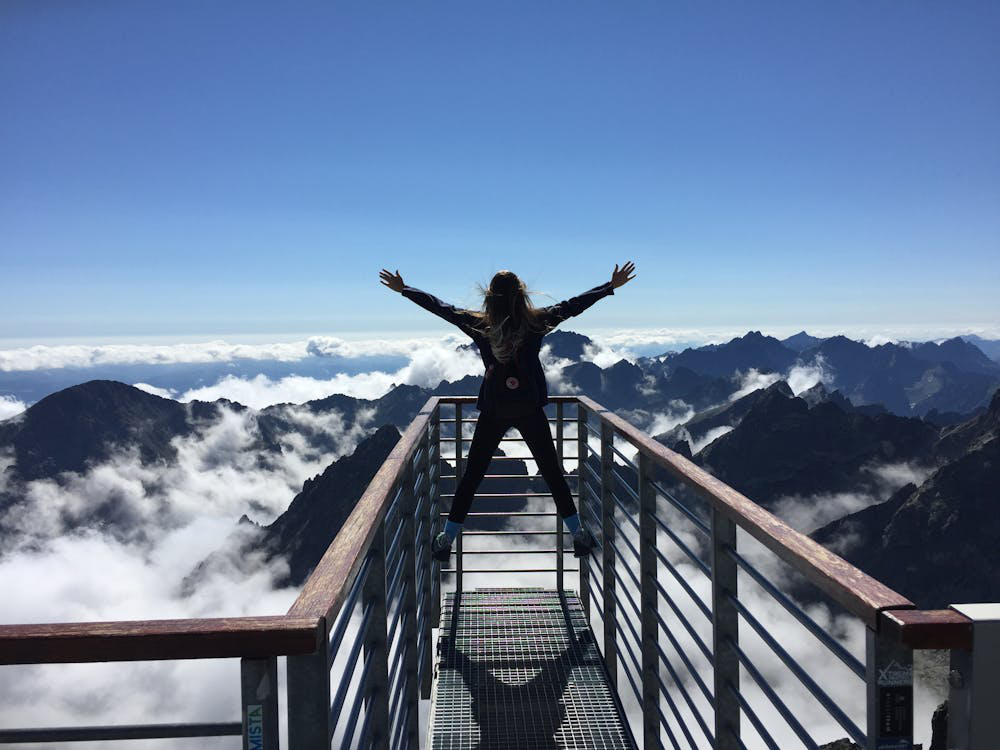 A woman standing with arms open, at a height facing mountains